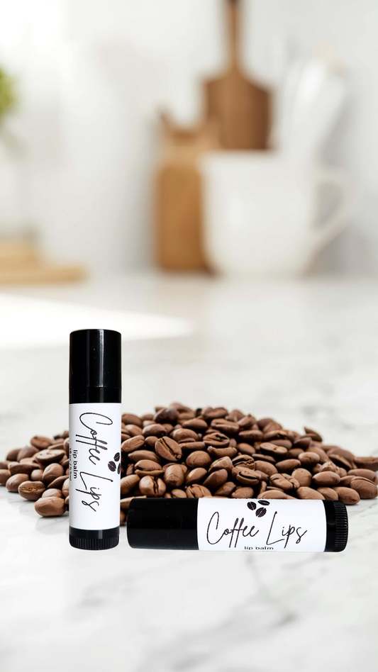 Two lip balm tubes labeled 'Coffee Lips' on a surface with coffee beans.